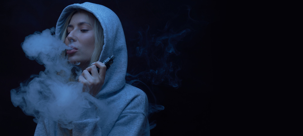 Woman vaping cbd and blowing vape cloud wearing a hoodie